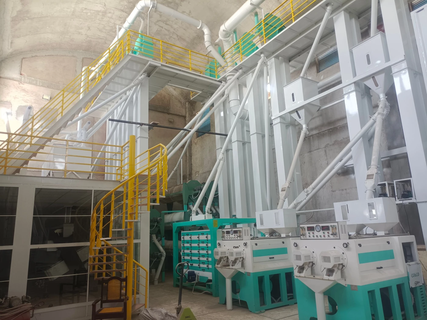 Tall elevator columns rising beside rice processing machines on two levels